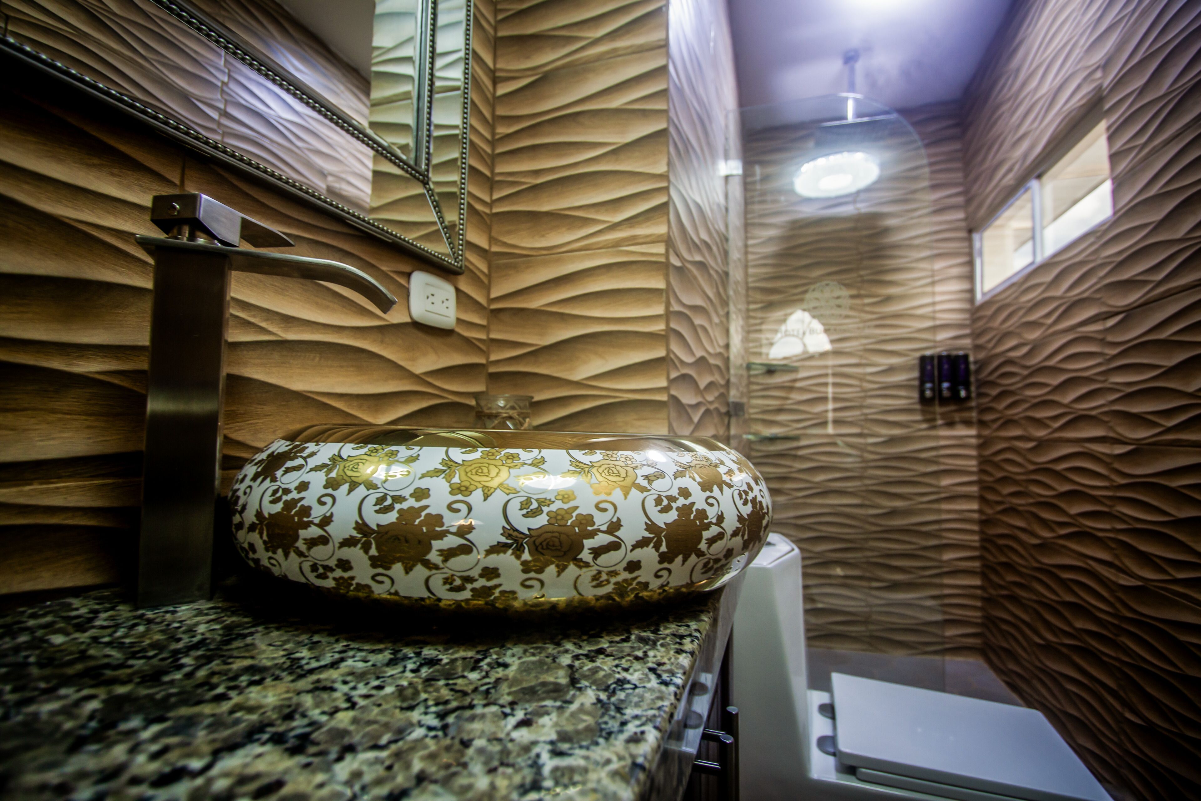A bathroom with a decorative sink, a mirror, and a textured wall.