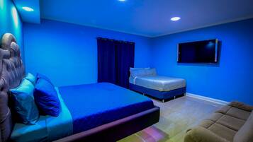 A bedroom with a large bed, a smaller bed, a TV mounted on the wall, and a chair.