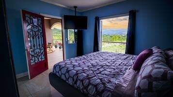 Een slaapkamer met een bed, een televisie, een balkon met uitzicht op groen en een deur met een nummer.
