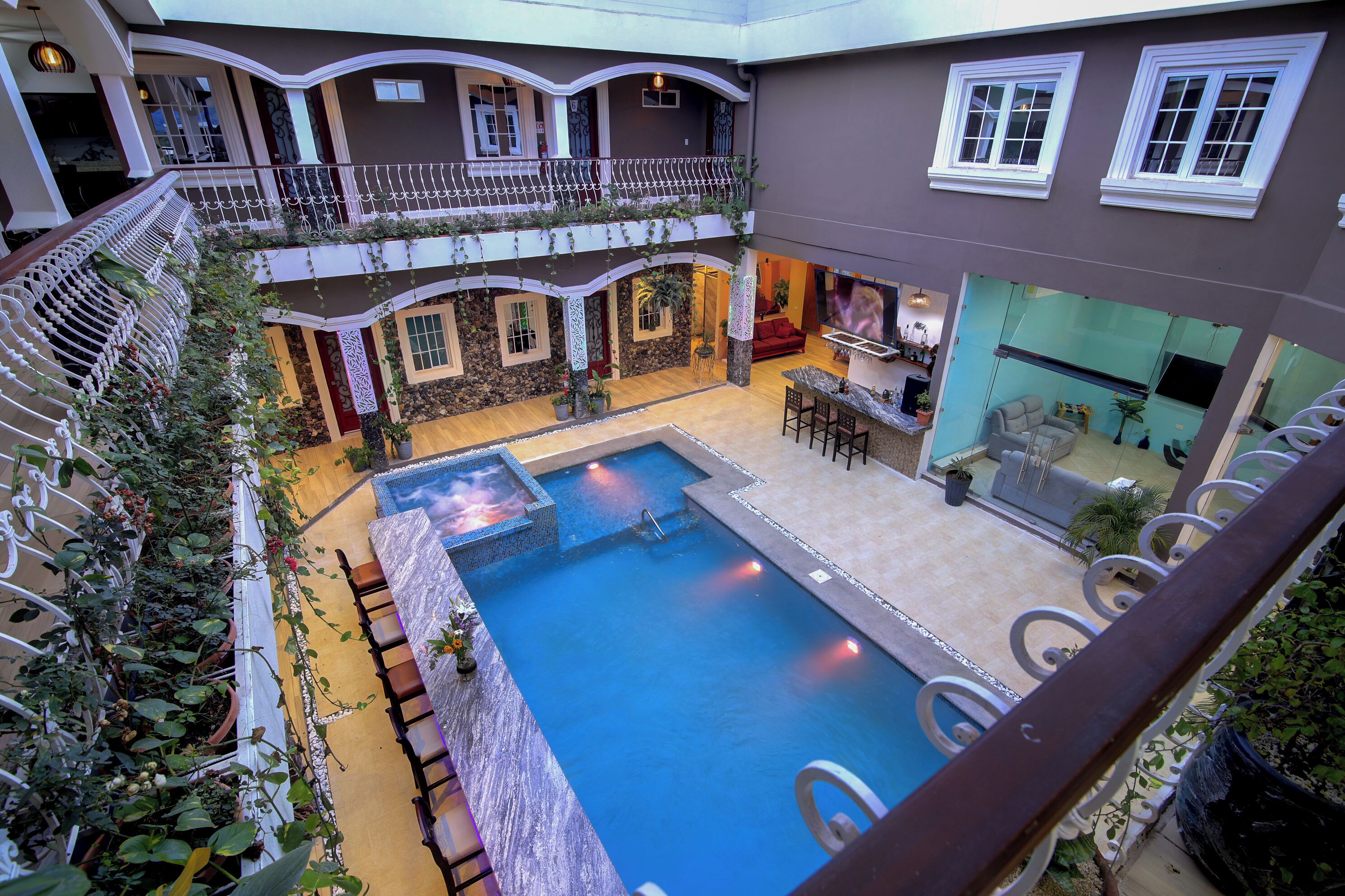 A multi-level indoor pool area with a central swimming pool, seating areas, and a balcony with a railing.