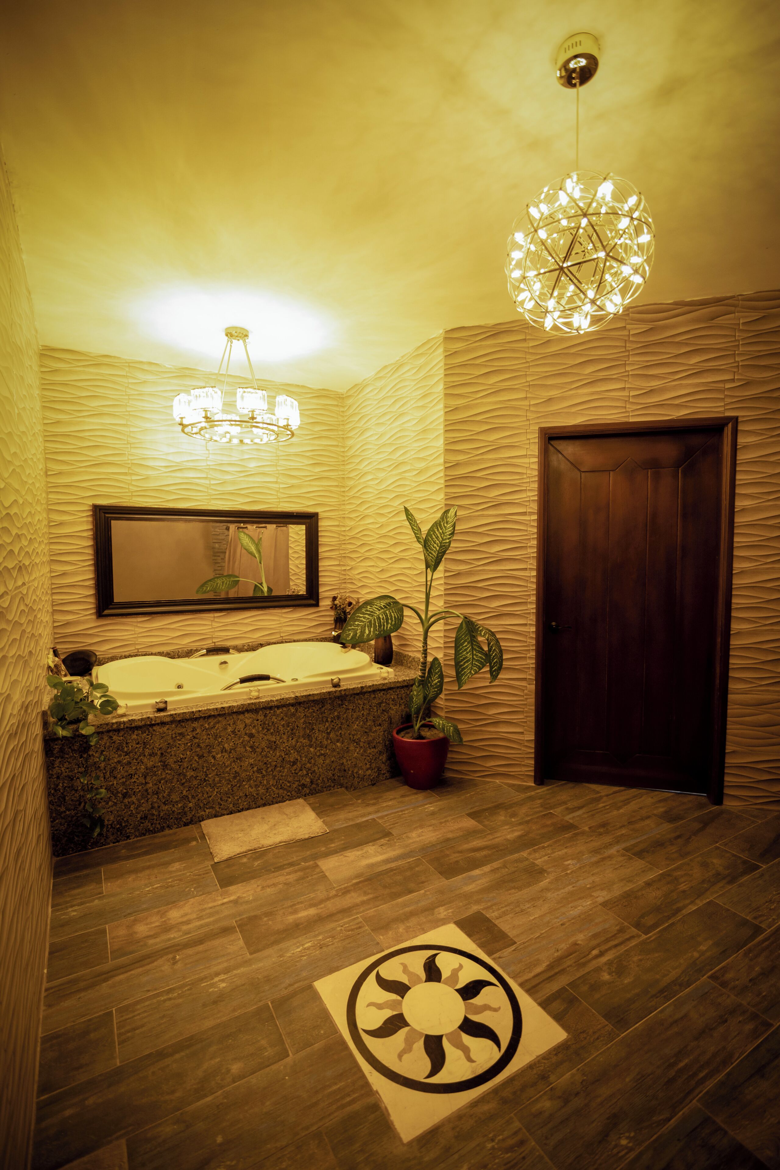 A bathroom with a bathtub, a mirror, a chandelier, a door, and a patterned floor.