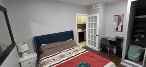 Ein Schlafzimmer mit Bett, Nachttisch, Lampe, Schreibtisch, Stuhl und Kleiderschrank.