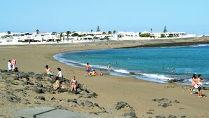 A beach with people sunbathing and swimming, white buildings in the background, and a clear sky. - La Casita de la Playa – A Vacation Just a Few Steps from the Ocean (Playa Honda)
