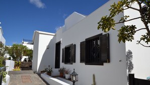 A narrow street with white buildings, black shutters, and potted plants. - La Casita de la Playa – A Vacation Just a Few Steps from the Ocean (Playa Honda)