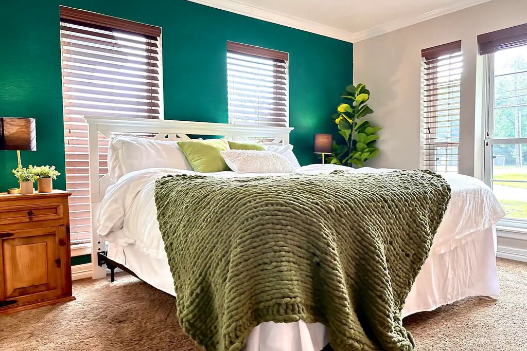 Un dormitorio con una cama, una mesita de noche, una lámpara y un ventanal con persianas.
