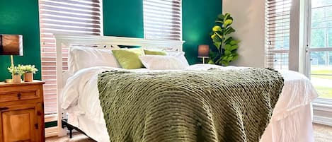 Un dormitorio con una cama, una mesita de noche, una lámpara y un ventanal con persianas.