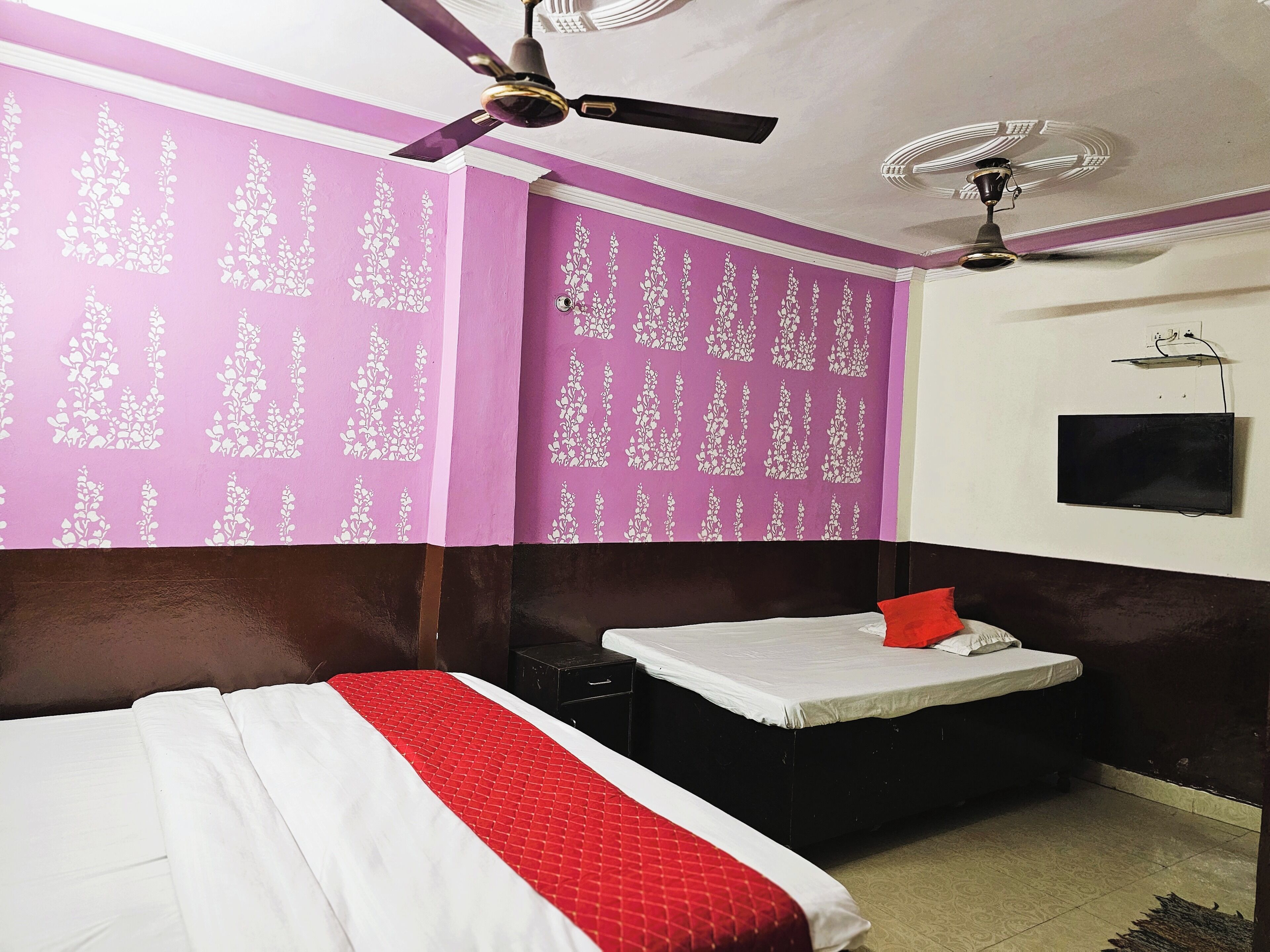 Um quarto com uma cama, uma mesinha, um ventilador de teto e uma TV fixada na parede.