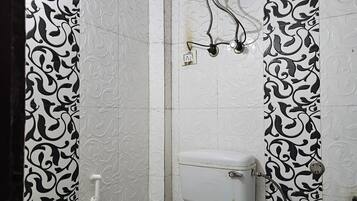 A bathroom with a toilet, a sink, and a shower with a damaged water tank.