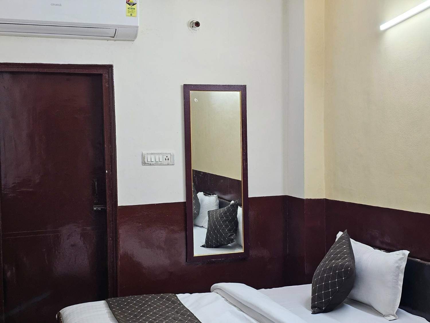 A hotel room with a bed, a mirror, a door, and an air conditioning unit.
