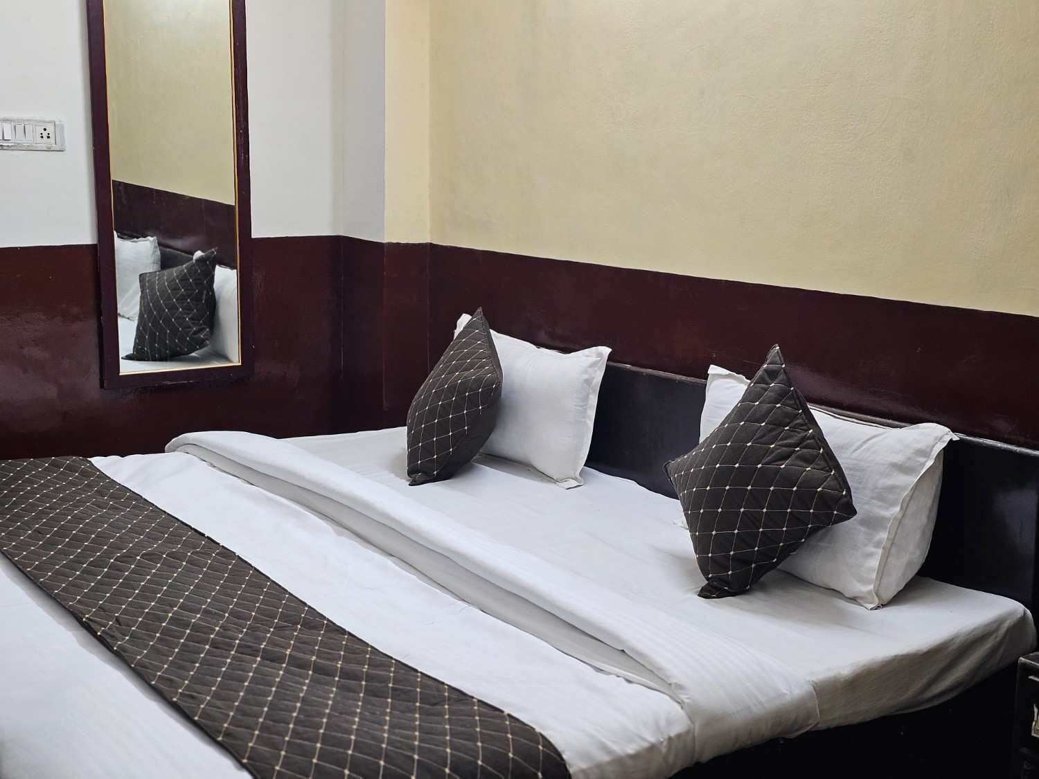 Habitación de hotel con cama, almohadas, manta, espejo y un enchufe.