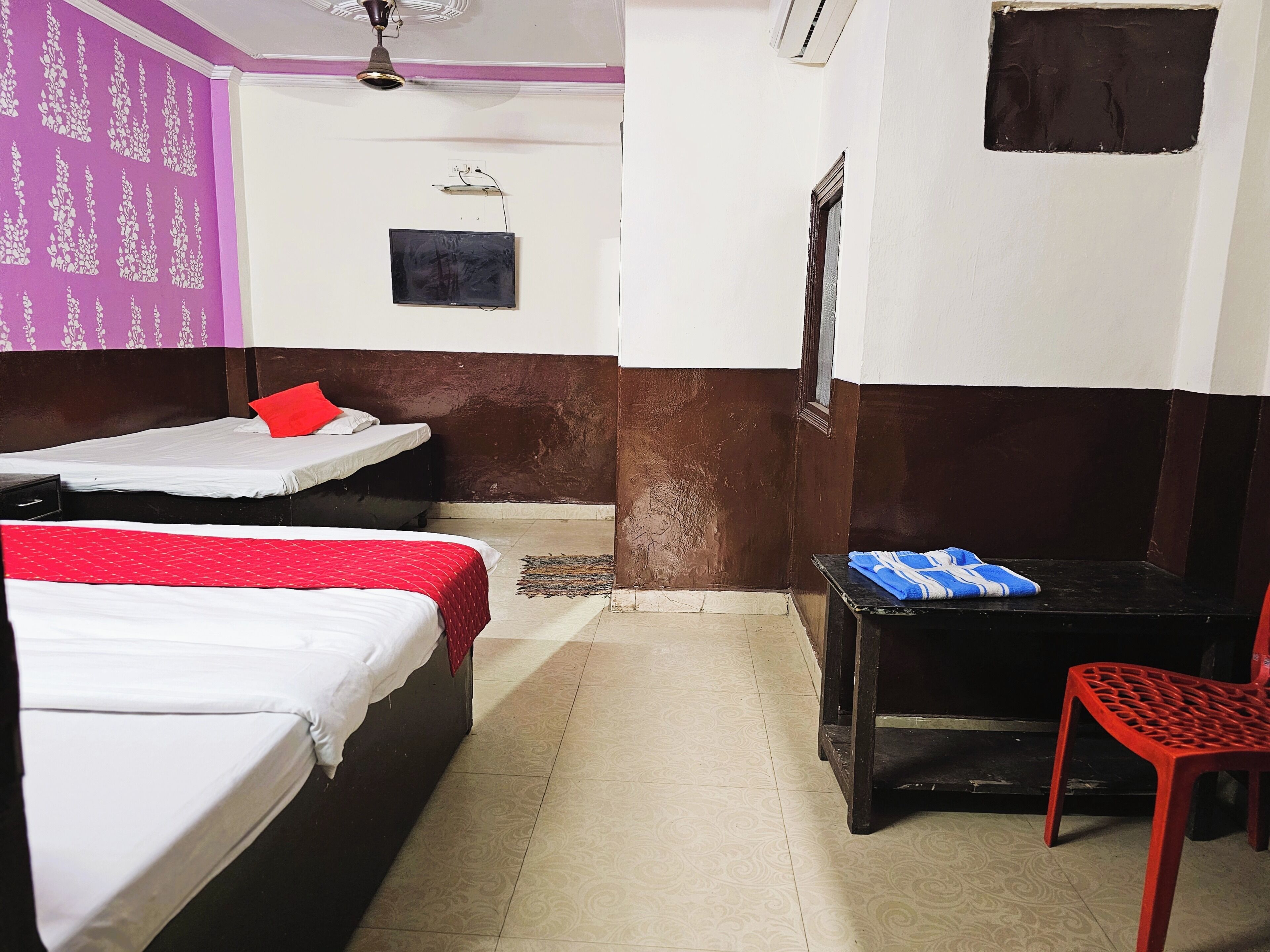 Une chambre avec deux lits, une petite table, une chaise, un ventilateur de plafond et un climatiseur fixé au mur.