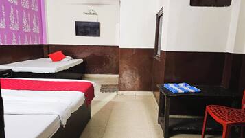 Une chambre avec deux lits, une petite table, une chaise, un ventilateur de plafond et un climatiseur fixé au mur.