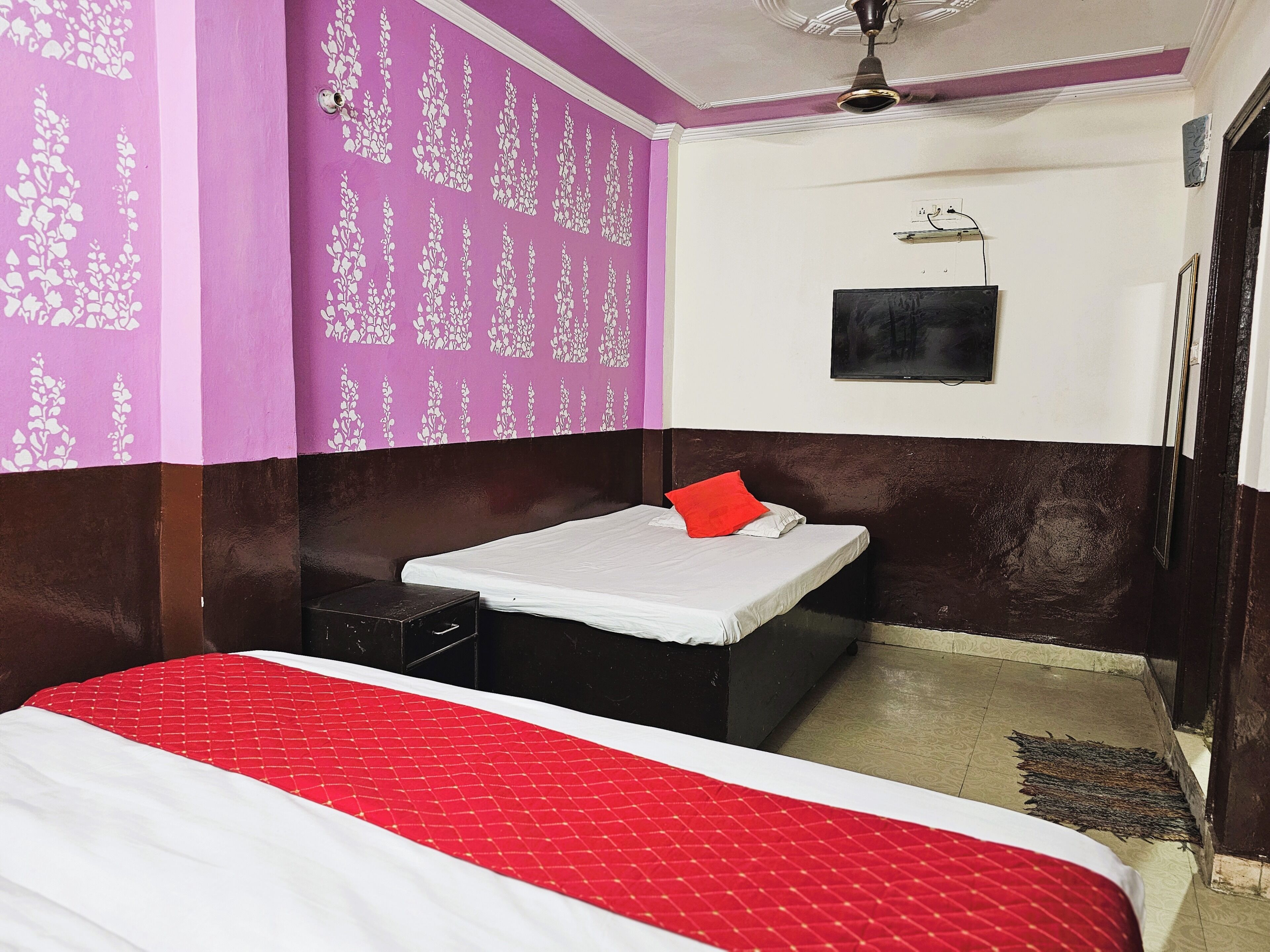 A room with a bed, a small table, a wall-mounted TV, and a ceiling fan.