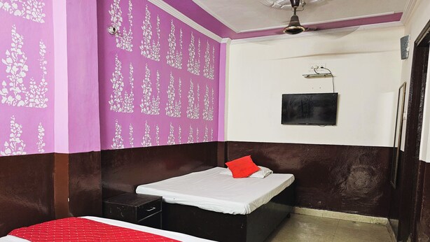 A room with a bed, a small table, a wall-mounted TV, and a ceiling fan.