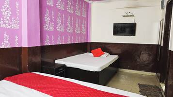 A room with a bed, a small table, a wall-mounted TV, and a ceiling fan.