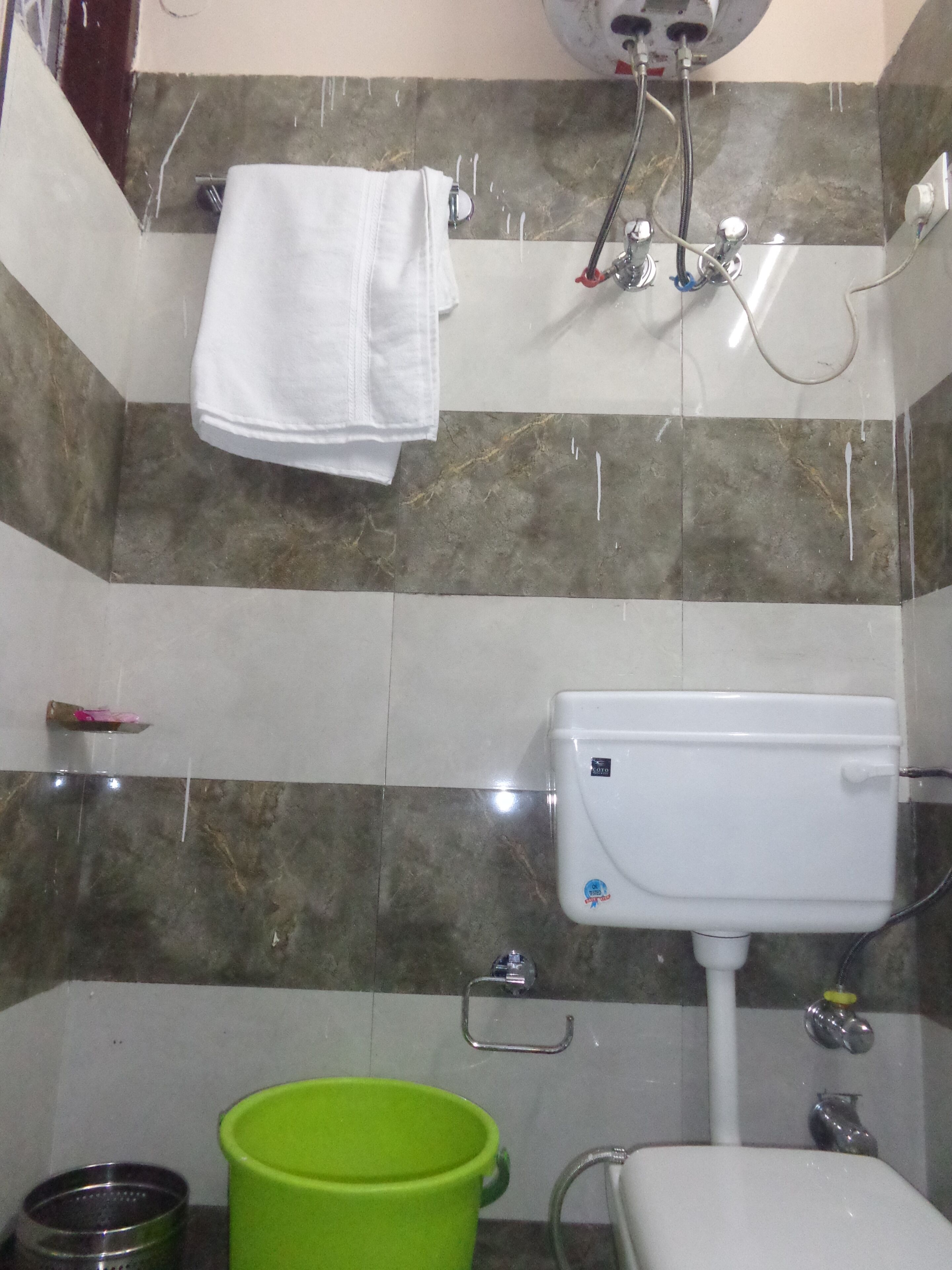 A bathroom with a toilet, a green bucket, and a towel hanging on the wall.