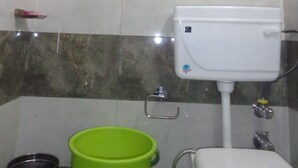 A bathroom with a toilet, a green bucket, and a towel hanging on the wall.