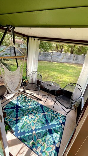 Ein überdachter Patio-Bereich mit einer Hängematte, zwei Stühlen und einem kleinen Tisch.