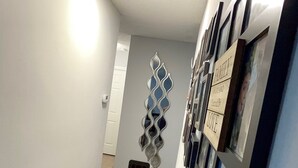 A hallway with a wooden floor, a light fixture on the ceiling, and a wall with a decorative mirror and framed pictures. - Serene Escape. Tropical Gem. 
Cozy Chic Condo, 
Shared space Pvt. Bed/Bath w AC (Eustis)