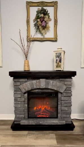 A fireplace with a stone surround, a framed picture above it, and a vase with branches on the mantel.