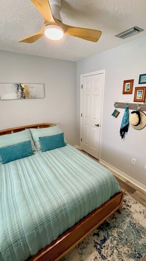 Un dormitorio con cama, ventilador de techo, una puerta y objetos montados en la pared.