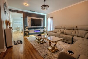 A modern living room with a flat-screen TV, a beige sofa, and a coffee table. - High End 4BR Luxury Family Home near Mercedes Benz Stadium, Sleeps 8 (Atlanta)