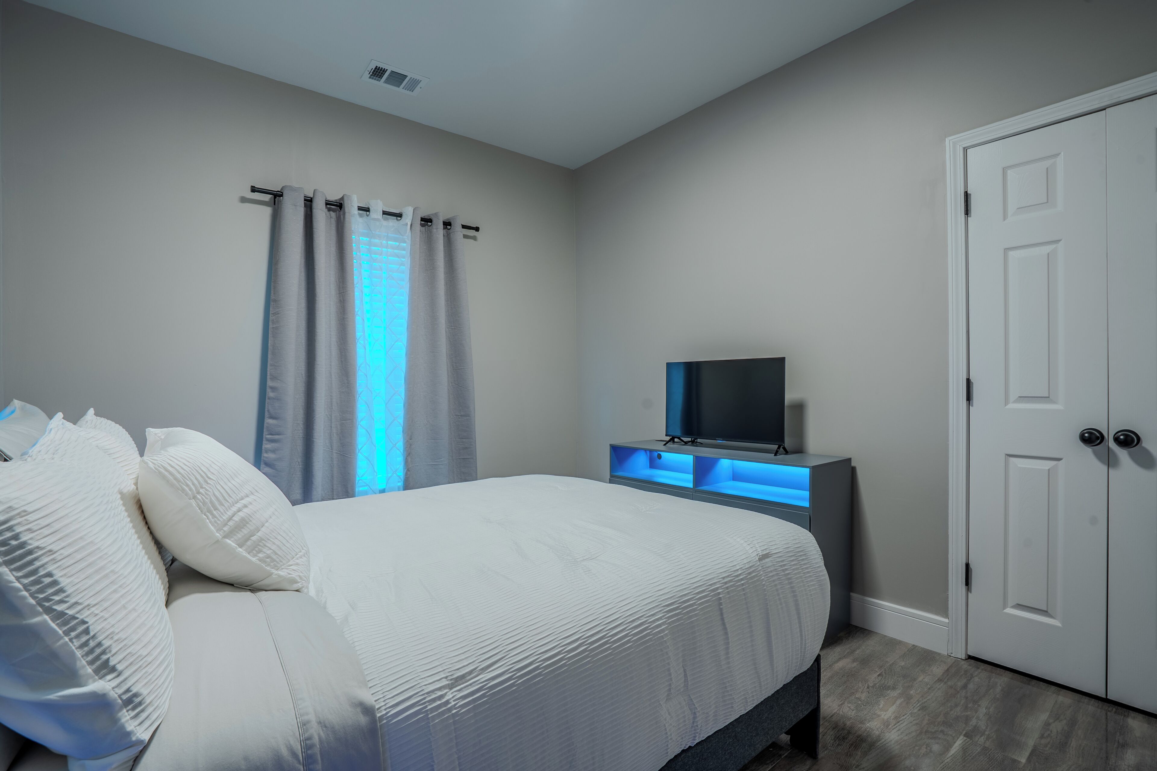 Un dormitorio con una cama, televisor sobre un mueble, una puerta y una ventana con cortinas.