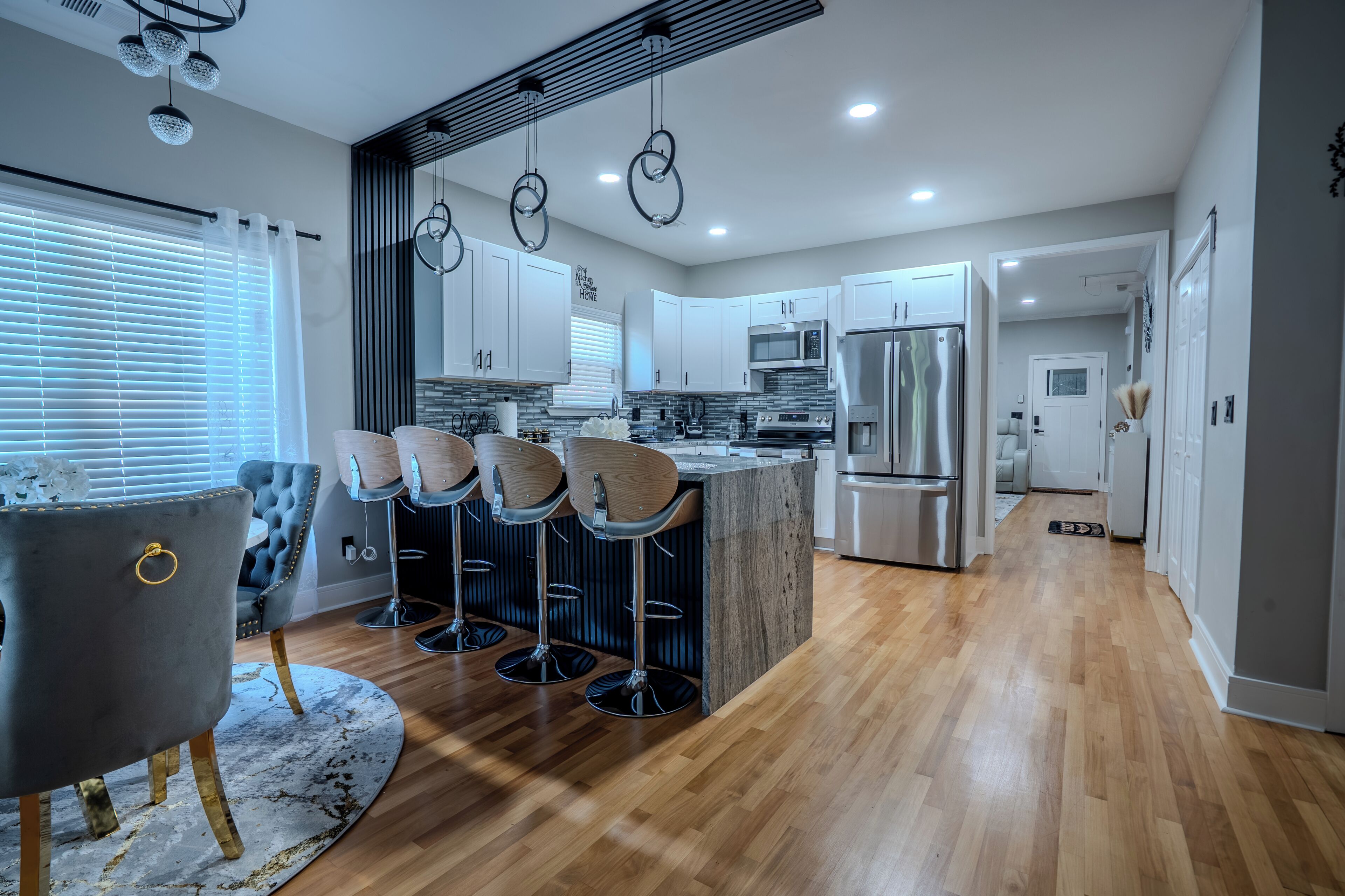 A modern kitchen with a central island, bar stools, and a grey upholstered chair.