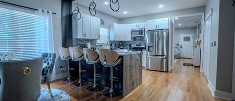 A modern kitchen with a central island, bar stools, and a grey upholstered chair.