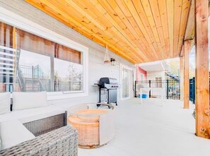 Ein überdachter Außenbereich mit Sitzgelegenheit, Grill und Blick auf ein Gebäude im Hintergrund.