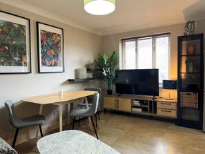 A modern living room with a flat-screen TV, a dining table, chairs, a sofa, and a bookshelf. - Brixton Apartment with Stylish Touches (London)