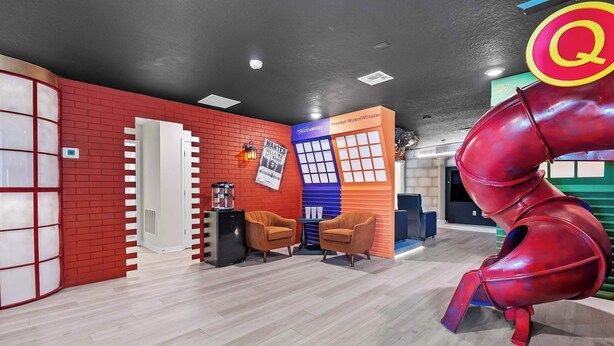 Un interior moderno con una pared de ladrillo rojo, una puerta blanca, un refrigerador negro, dos sillas naranjas y una encimera azul y naranja.