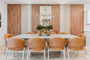 A dining area with a rectangular table, six upholstered chairs, a chandelier, and two vases with plants. - Luxury 8BR Themed Villa with Private Pool (Clermont)