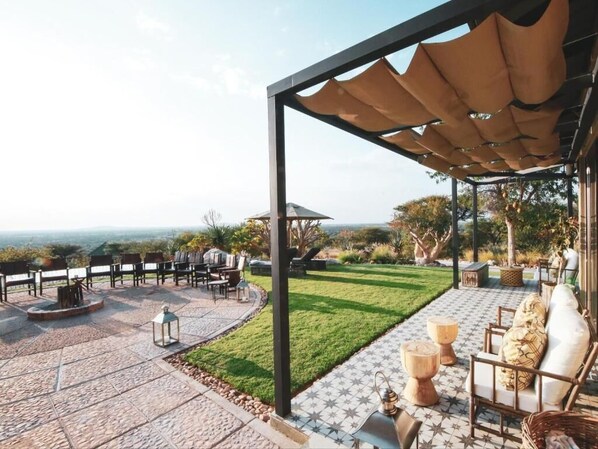 An outdoor patio with a view, furnished with chairs and tables, and a pergola providing shade.