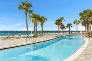 A swimming pool with lounge chairs and palm trees, a pier in the background, and a clear blue sky. - Thunder Beach🏍️! Rally, Recharge, Repeat! Calypso 2 • 19 Floors Above the Surf 🌊 (Panama City Beach)
