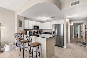 A modern kitchen with white cabinets, stainless steel appliances, and a central island with bar stools. - Thunder Beach🏍️! Rally, Recharge, Repeat! Calypso 2 • 19 Floors Above the Surf 🌊 (Panama City Beach)