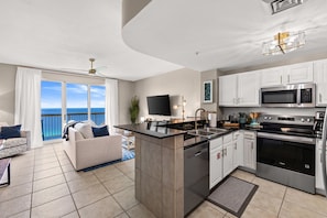 A modern kitchen with a central island, white cabinetry, and stainless steel appliances. - Enjoy Luxe King Mattress after Iron Man 💪Calypso II beachfront 19th Floor View! (Panama City Beach)