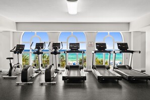 A gym with treadmills, elliptical machines, and stationary bikes, with a view of the beach through large windows. - Enjoy Luxe King Mattress after Iron Man 💪Calypso II beachfront 19th Floor View! (Panama City Beach)