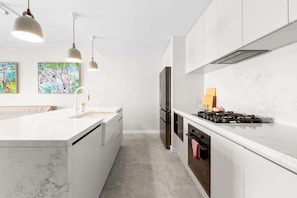A modern kitchen with white cabinetry, a central island, a built-in stove, and pendant lighting. - Designer 2BR Terrace | BBQ Garden near Moore Park (Redfern)