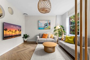 A modern living room with a sofa, a coffee table, and a painting of a sunset. - Designer 2BR Terrace | BBQ Garden near Moore Park (Redfern)