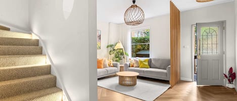 A staircase with a textured carpet, a living room with a sofa, a round coffee table, and two hanging light fixtures.