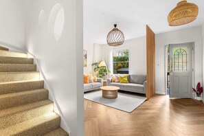 A staircase with a textured carpet, a living room with a sofa, a round coffee table, and two hanging light fixtures. - Designer 2BR Terrace | BBQ Garden near Moore Park (Redfern)