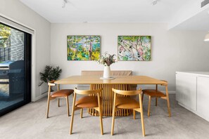A modern dining area with a wooden table and six chairs, two paintings on the wall, and a vase with flowers on the table. - Designer 2BR Terrace | BBQ Garden near Moore Park (Redfern)