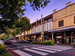 A street view with a pedestrian crossing, parked cars, and buildings with storefronts. - Designer 2BR Terrace | BBQ Garden near Moore Park (Redfern)