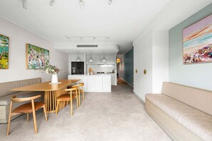 A modern kitchen with white cabinets, a central island, pendant lighting, and a dining area with a wooden table and chairs. - Designer 2BR Terrace | BBQ Garden near Moore Park (Redfern)