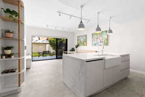 A modern kitchen with a marble island, pendant lighting, and a view to the outdoor patio. - Designer 2BR Terrace | BBQ Garden near Moore Park (Redfern)