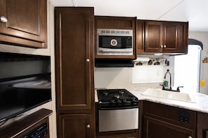 A compact kitchen with a built-in microwave, stove, and sink. - Modern RV on the shores of Maria Lake. (Walsenburg)