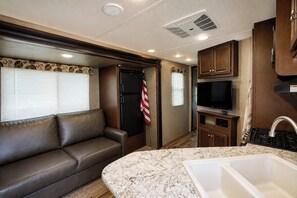 A compact RV interior with a kitchenette, a seating area, and a door with an American flag.
