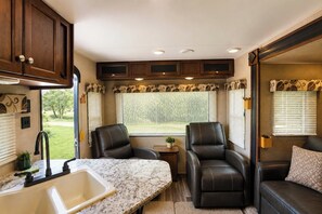 A compact RV interior with a kitchen area, two seating options, and a window providing natural light.