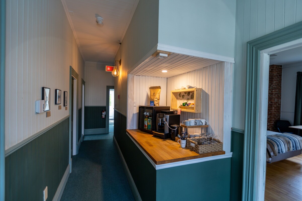 A narrow hallway with a wooden counter, a coffee machine, and a basket of glasses.